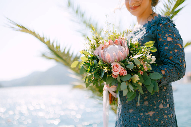 The bride in a stylish gray dress stands with wedding bouquets on the seashore, close-up - Photo, Image