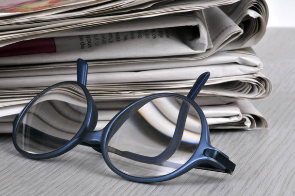 Glasses resting next to a stack of newspapers  - Photo, Image