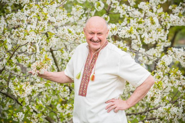 Çiçek bahçesinde nakışlı gömlekli yaşlı adam. - Fotoğraf, Görsel