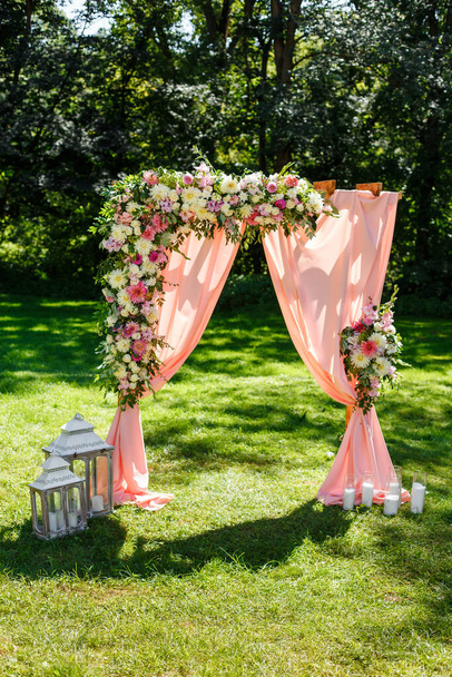 公園内の結婚式のエリア。木製の長方形のアーチ、花、緑、花弁、葉や桃の色のチュールで飾られた白い椅子。かわいい、トレンディーな素朴な装飾 - 写真・画像