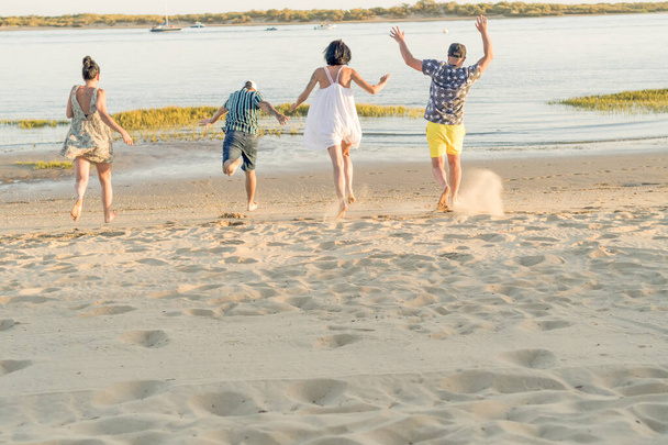 achteraanzicht van jonge vrienden die spelen en plezier hebben terwijl ze rennen en springen op het strand op vakantie. zomeractiviteit. vriendschap, plezier en eenheid - Foto, afbeelding