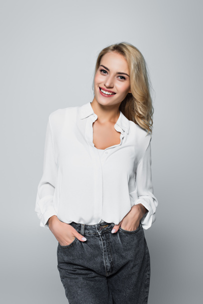 happy young woman posing with hands in pockets isolated on grey - Foto, Imagen