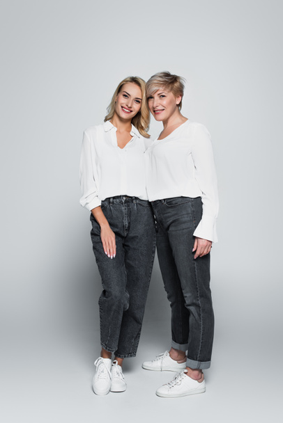 full length view of stylish mother and daughter looking at camera while posing on grey - Photo, Image