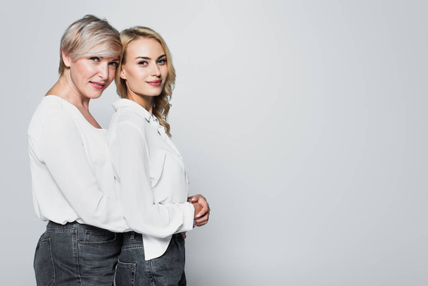 mature woman embracing adult daughter while looking at camera isolated on grey - Foto, immagini