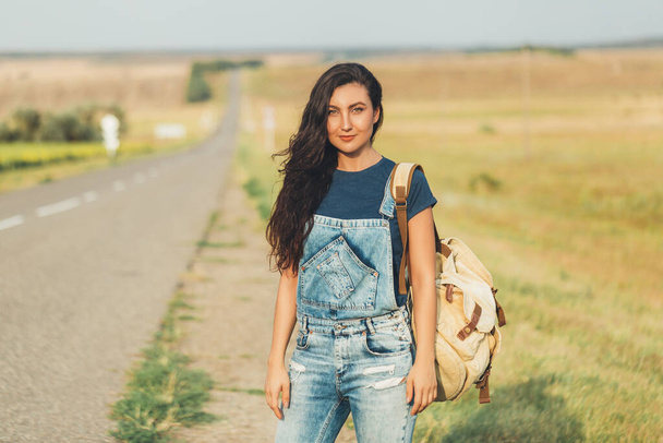 Brunette with backpack waiting for bus on road. Lifestyle, countryside, travel. Copy space - Foto, Imagem