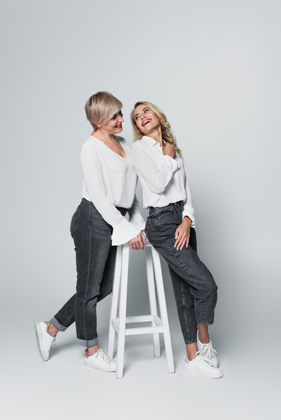 full length view of trendy mother and daughter looking at each other near high chair on grey - Zdjęcie, obraz