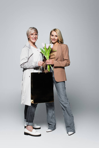 happy mother and daughter with shopping bag and tulips on grey - Fotó, kép