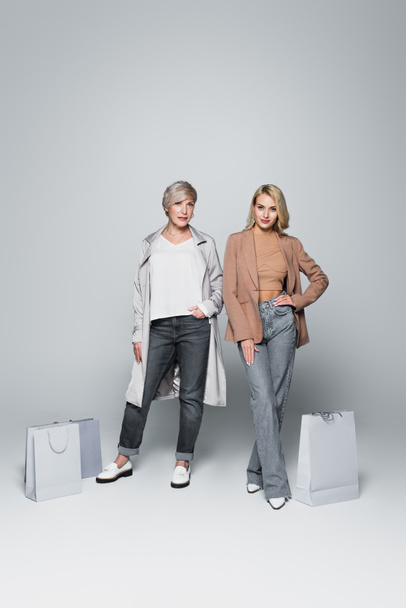mother and daughter in trendy clothes posing near shopping bags on grey - Photo, image