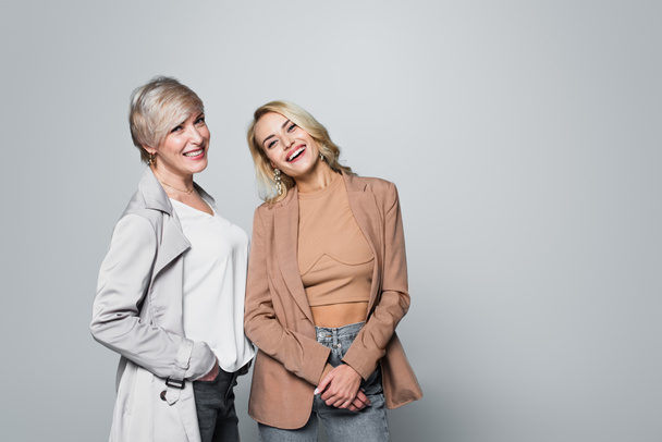 joyful, stylish mother and daughter smiling at camera isolated on grey - Fotografie, Obrázek