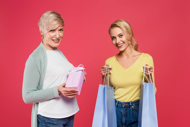 happy, stylish mother and daughter smiling at camera while holding presents isolated on pink - Φωτογραφία, εικόνα