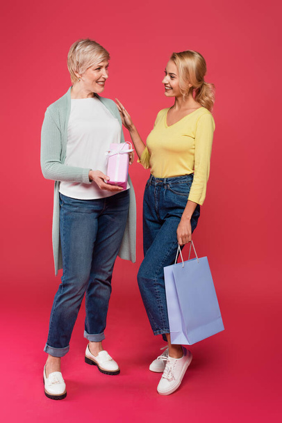 full length view of joyful mother and daughter holding presents while standing on pink - Foto, afbeelding