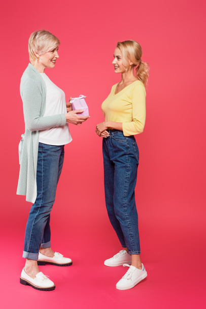 full length view of stylish, middle aged woman holding present near young daughter on pink - Photo, Image