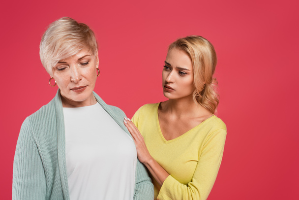worried woman touching offended mother isolated on pink - Foto, afbeelding