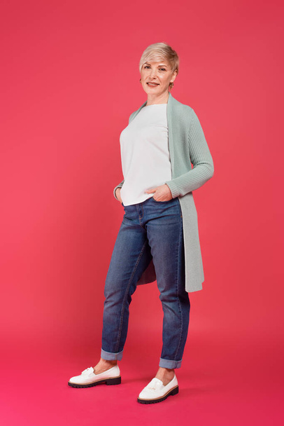 повнометражний вид на модну жінку, позує руками в кишенях джинсів на рожевому
 - Фото, зображення