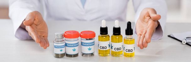 bijgesneden beeld van Afrikaanse Amerikaanse arts wijzend met de handen op flessen met medicinale cannabis en cbd, banner - Foto, afbeelding