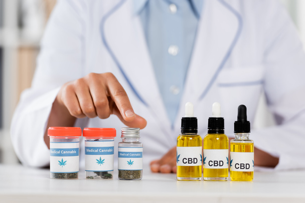 cropped view of doctor pointing with finger at bottles with legal cbd and medical cannabis  - Photo, Image