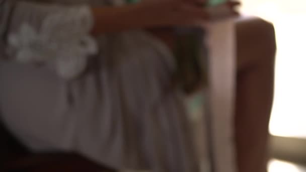 Μια γυναίκα με μεταξωτή ρόμπα κρατά ένα νυφικό μπουκέτο στην αγκαλιά της και παίζει με μακριές κορδέλες - Πλάνα, βίντεο