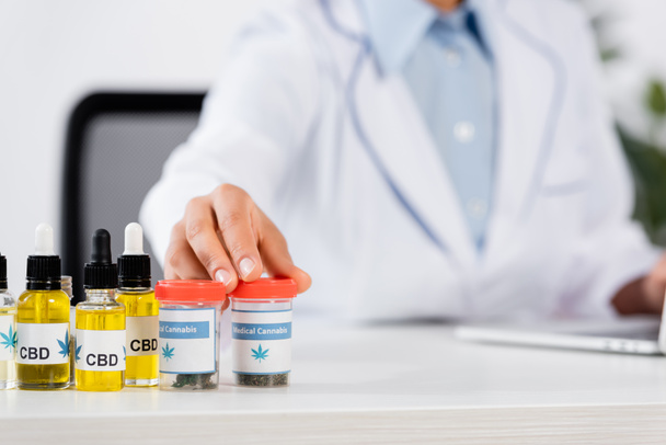 cropped view of blurred doctor reaching bottles with medical cannabis and cbd lettering on table  - Photo, Image