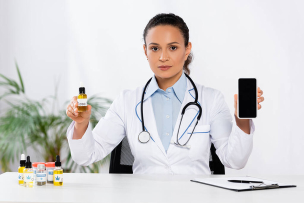 medico afroamericano bottiglia con cbd e smartphone con schermo bianco - Foto, immagini