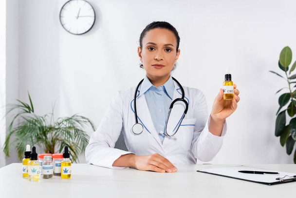african american doctor holding bottle with cbd lettering in clinic - Photo, Image