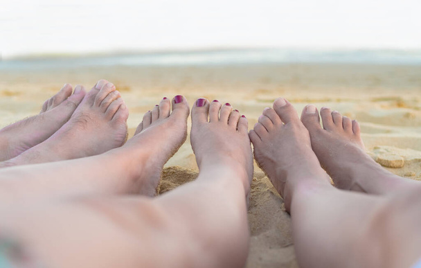 groep vrienden voeten rusten en ontspannen op het strand met de oceaan op de achtergrond. vakantie en vriendschap concept. - Foto, afbeelding