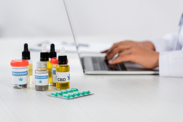 обрезанный вид африканского американского врача, печатающего на ноутбуке рядом с лекарством от конопли на столе - Фото, изображение