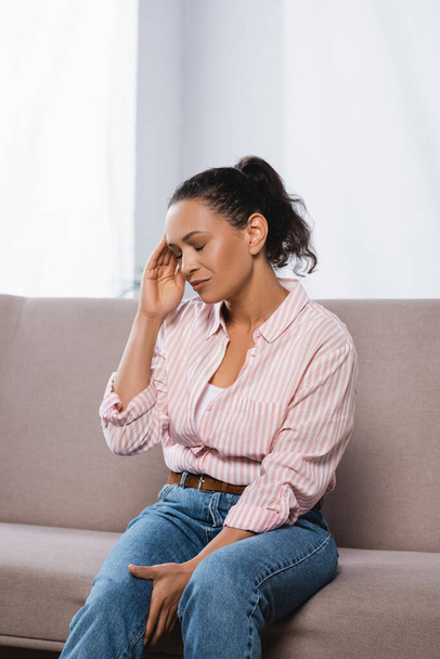 Afrikanische Amerikanerin leidet unter Kopfschmerzen, während sie auf der Couch sitzt  - Foto, Bild