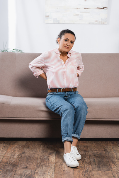afro-amerikai nő szenved hátfájás, miközben ül a kanapén - Fotó, kép