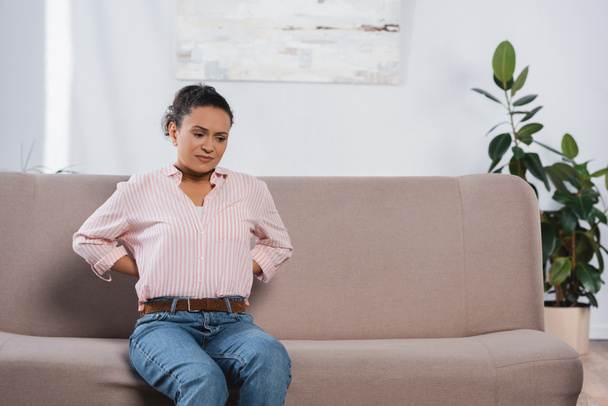 donna afro-americana che soffre di mal di schiena mentre è seduta sul divano - Foto, immagini