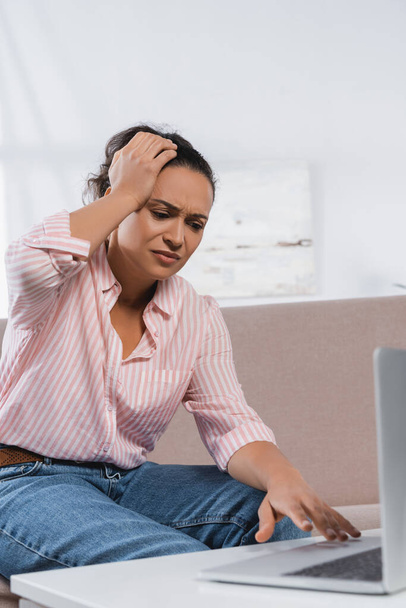 afro-américaine pigiste souffrant de maux de tête et utilisant un ordinateur portable dans le salon  - Photo, image