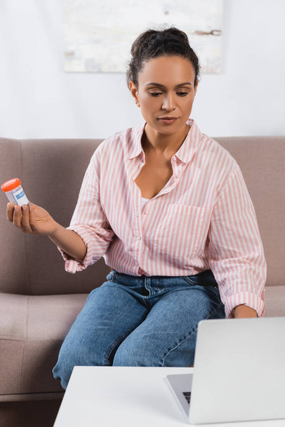 Afrikkalainen amerikkalainen freelancer käyttäen kannettavaa tietokonetta ja pitämällä pullon lääkekannabiksen - Valokuva, kuva