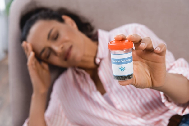 hämärtynyt afrikkalainen amerikkalainen nainen kärsii migreeni ja pitämällä pullon lääkekannabiksen olohuoneessa - Valokuva, kuva