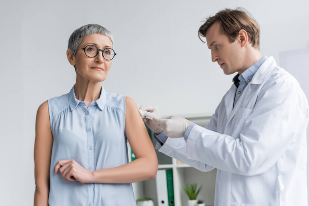 Arzt im Mantel impft Frau in Klinik  - Foto, Bild