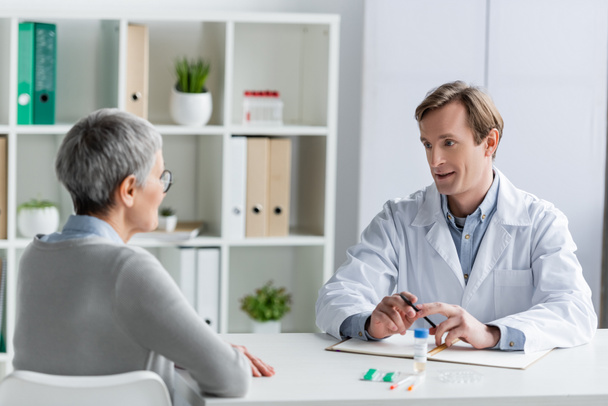 Lekarz rozmawia z pacjentem w pobliżu notebooka i szczepionki - Zdjęcie, obraz