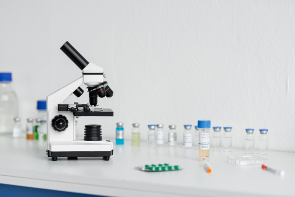 Mikroskooppi rokotteiden ja ruiskujen läheisyydessä epäselvällä etualalla laboratoriossa  - Valokuva, kuva