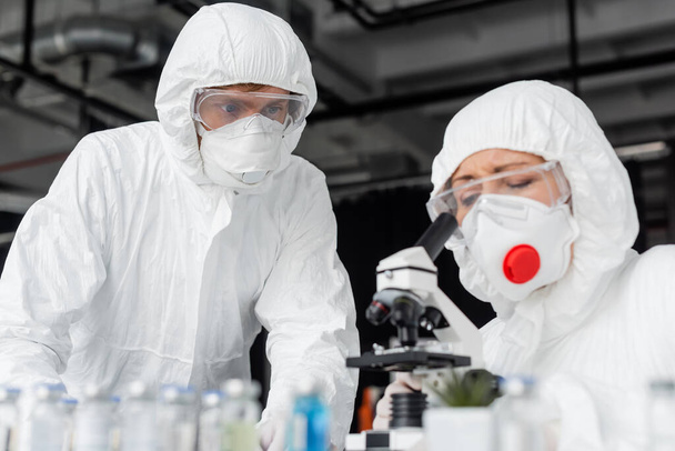 Scientist standing near colleague using microscope and vaccines on blurred foreground  - Photo, Image