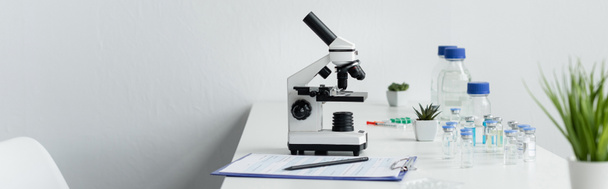 Portapapeles cerca del microscopio y vacunas en laboratorio, pancarta  - Foto, Imagen
