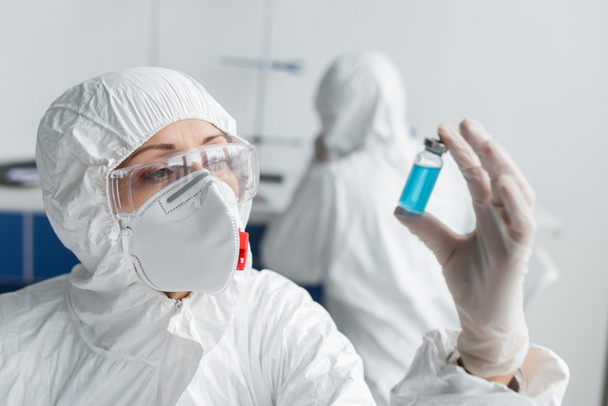 Wetenschapper houdt pot met vaccin op wazige voorgrond tijdens het werken in laboratorium  - Foto, afbeelding