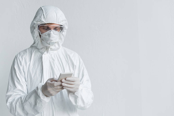 Scientist in hazmat suit using smartphone near wall - Φωτογραφία, εικόνα