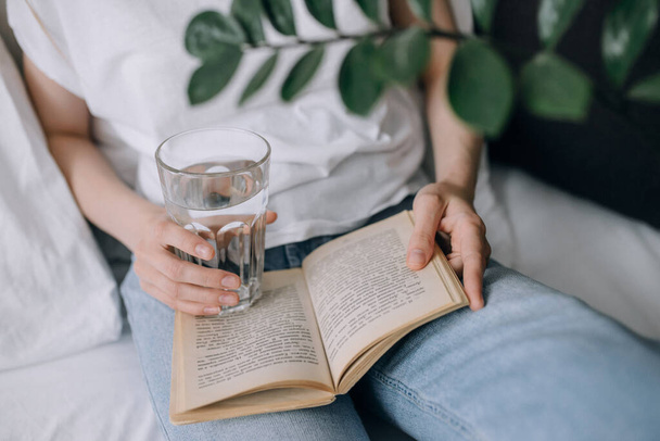 Mujer joven leyendo un libro y sosteniendo un vaso de agua de cerca - Foto, imagen
