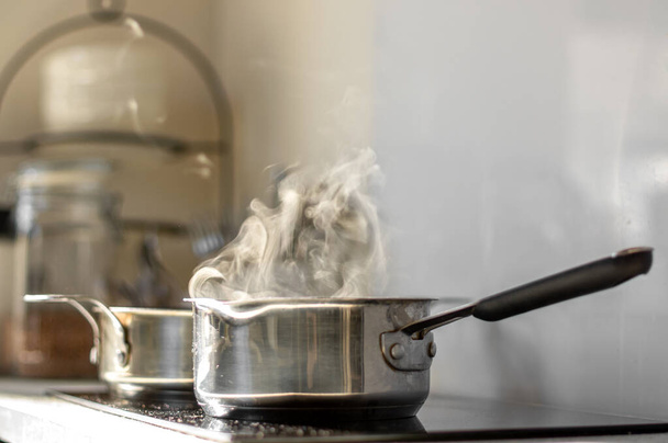 Forró víz gőzzel egy edényben egy elektromos tűzhelyen a konyhában. Homályos háttér. Szelektív fókusz. - Fotó, kép