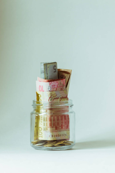 Un piccolo barattolo di vetro con i soldi si erge su uno sfondo bianco primo piano. - Foto, immagini