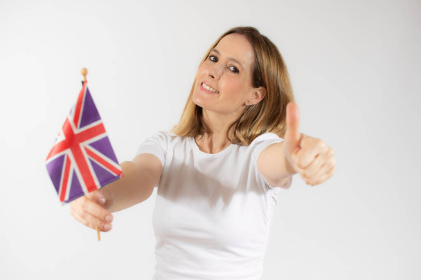 Портрет улыбающейся девушки, держащей британский флаг с большим пальцем на белом фоне - Фото, изображение