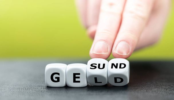 Рука повертає кості і змінює німецьке слово "Geld" (гроші) на "Gesund" (здоров'я). - Фото, зображення