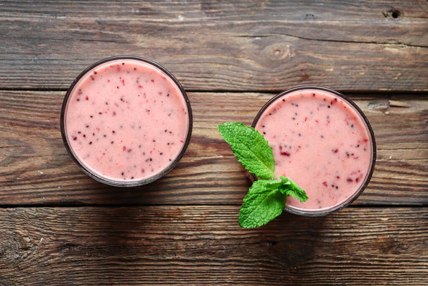 Berry yogurt with mint in a glass. Fruit and berry smoothie. The milkshake is pink. Healthy eating. Copy space. Top view. Wood background - Photo, Image