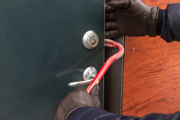 Ladrón usando guantes negros rompiendo en una casa con herramienta. - Foto, Imagen