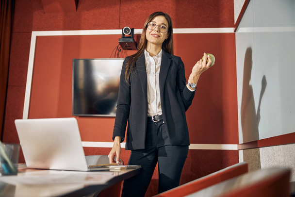 Trabajador de oficina sonriente en un traje pantalón de pie en el escritorio - Foto, Imagen