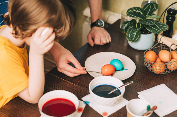 Easter day. Father and son painting eggs on wooden background. Family sitting in a kitchen. Preparing for Easter, creative homemade decoration - Photo, Image