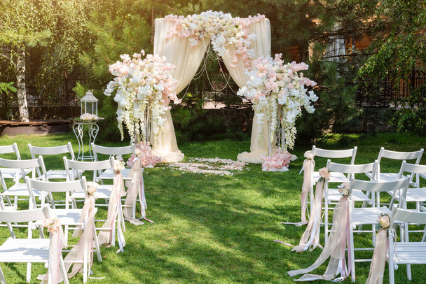 Svatební oblouk zdobený látkou a květinami venku. Krásná svatební aranžmá. Svatební obřad na trávníku v zahradě. Součástí slavnostní výzdoby, květinové aranžmá - Fotografie, Obrázek