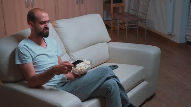 Hombre concentrado sentado frente a la televisión usando control remoto - Imágenes, Vídeo